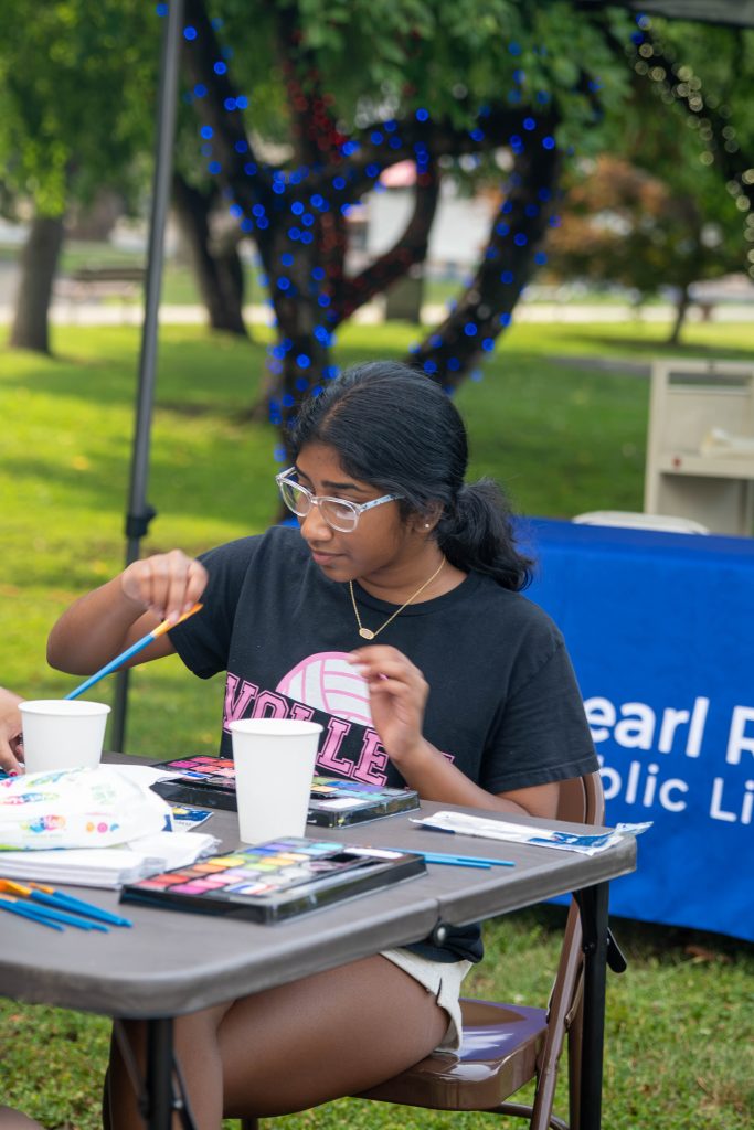 A young girl paints at a table during an outdoor event