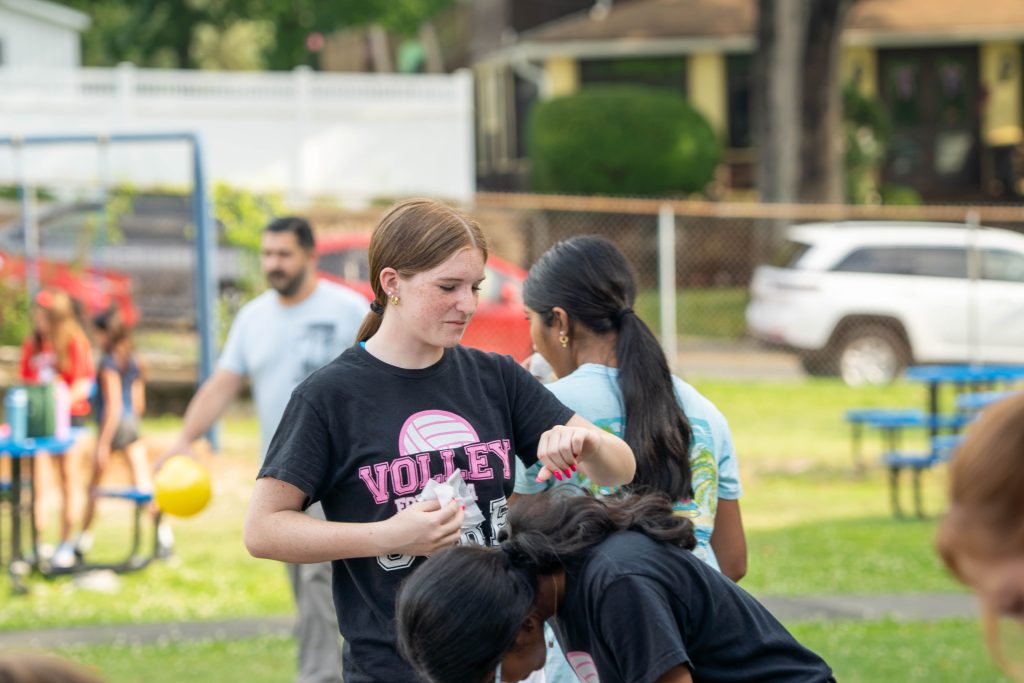 A girl in a volleyball shirt interacts with friends outdoors