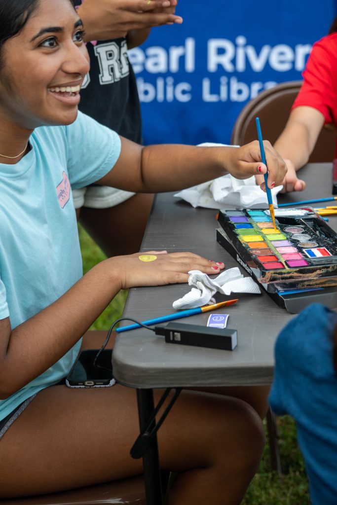 A young woman paints colorful designs on her hand at a table