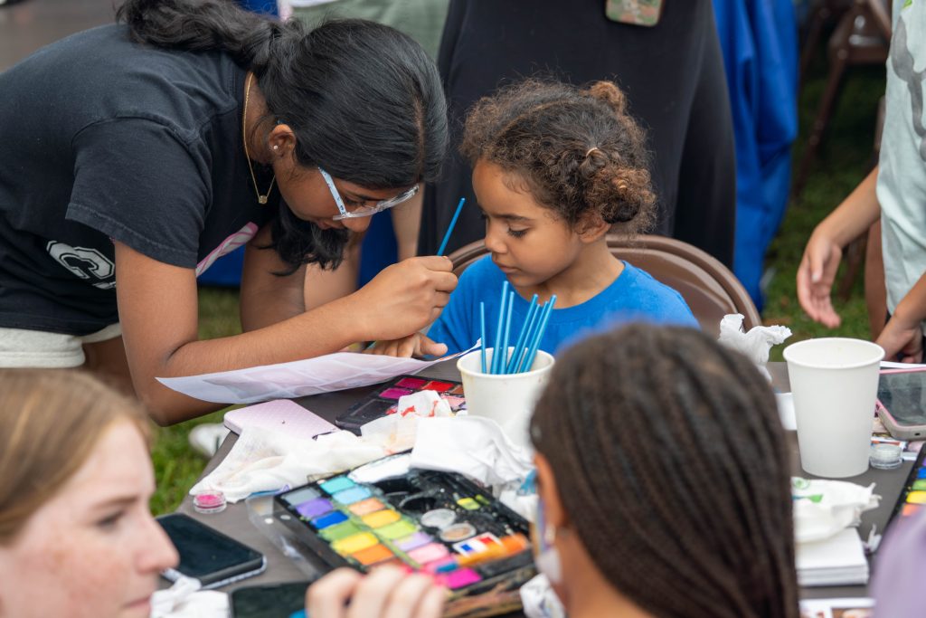 A young girl receives face painting at a community event