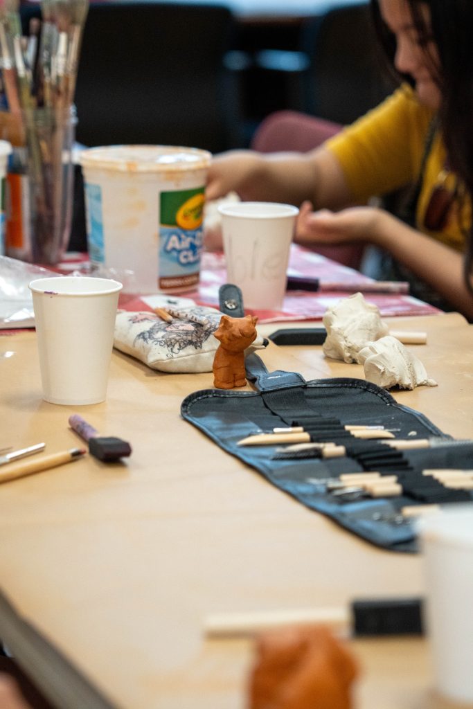 A small clay figure sits on a crafting table with tools