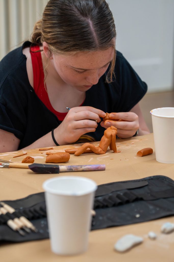 A young artist carefully sculpts a clay figure at a table