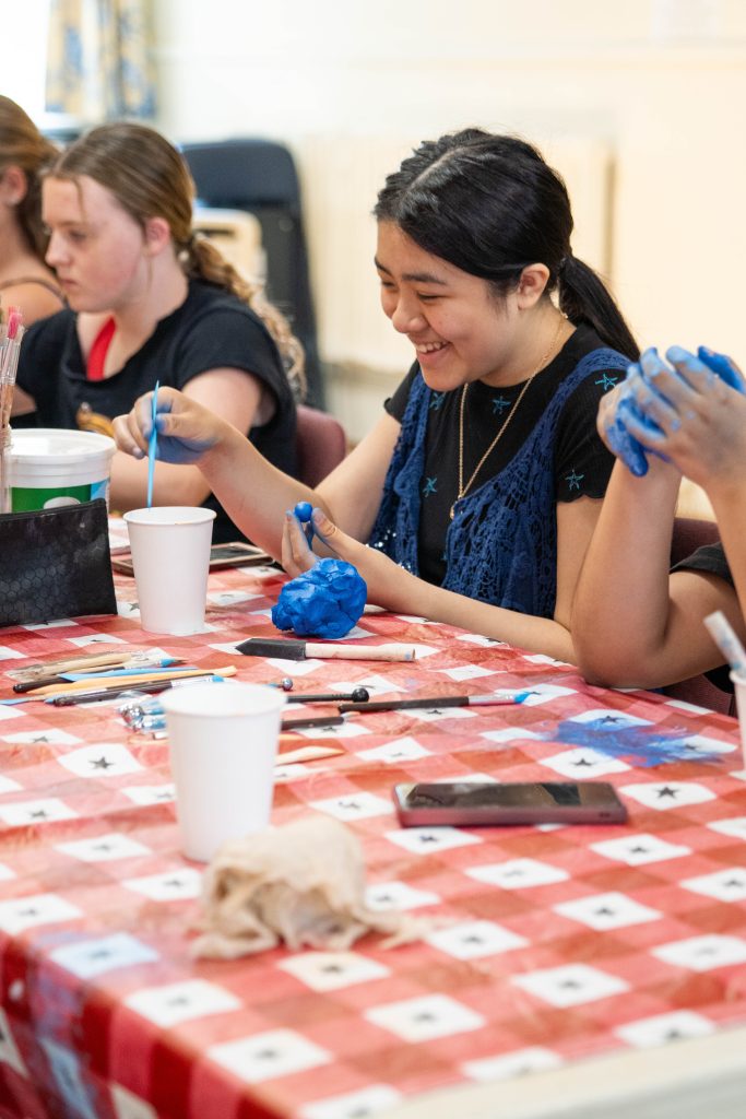 A girl smiles while shaping blue clay at a crafting table