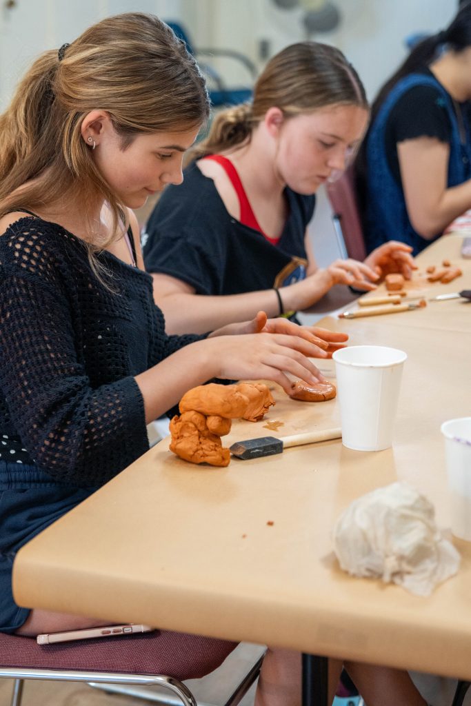 Two girls sculpting with orange clay at a table