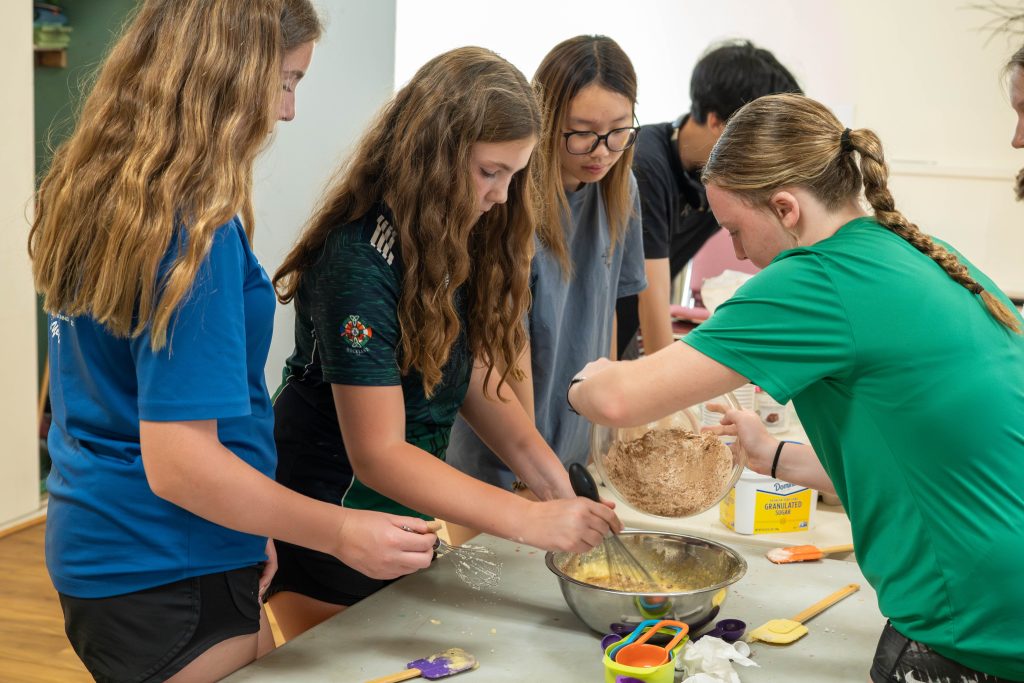 Four young people baking together, mixing ingredients in a bowl
