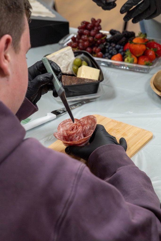 A person shapes salami into a rose on a cutting board