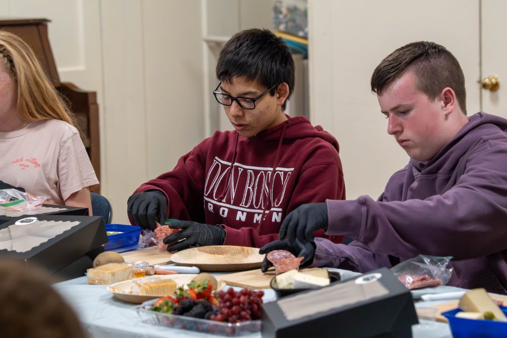 Two young people preparing a charcuterie board at a table